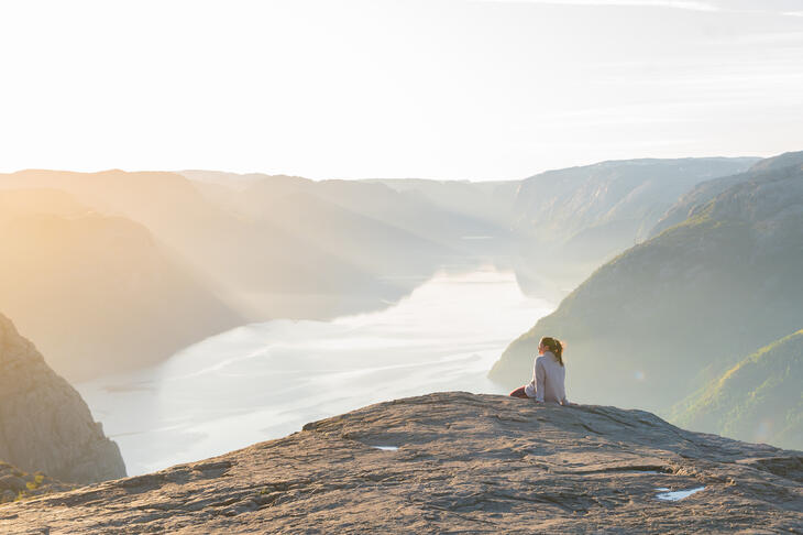 Person sitting on the edge of the Preikestolen (Pulpit Rock) with fjord views below