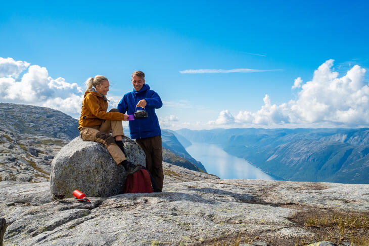 Two people on top of a mountain with a fjord in the background