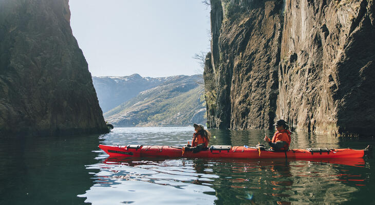 Two people in a kayak in a fjord with mountains on both sides