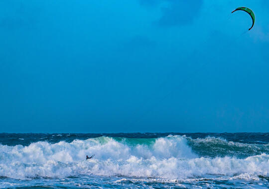 Blått hav og bølger med hvite topper og en kiter.