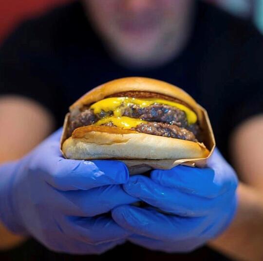 To hanskekledde hender viser frem en burger