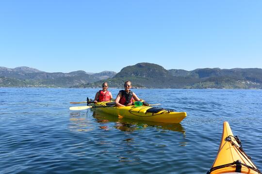 Two girls in a yellow kayak during a guided tour on the water outside Jørpeland, with mountains in the background.