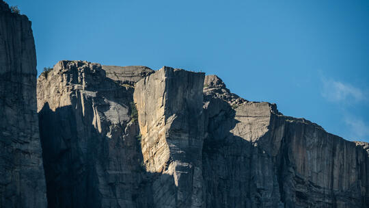 Preikestolen- a mountain formation seen from below in the fjord. Grey mountain sides and blue sky.