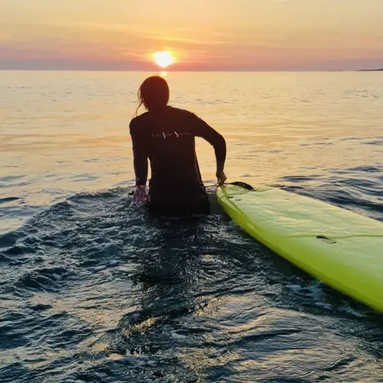 Dame i solnedgang med surfebrett på vei ut i sjøen.