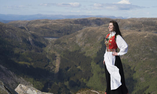 Woman dressed in typical Norwegian dress bunad with mountains surrounding her