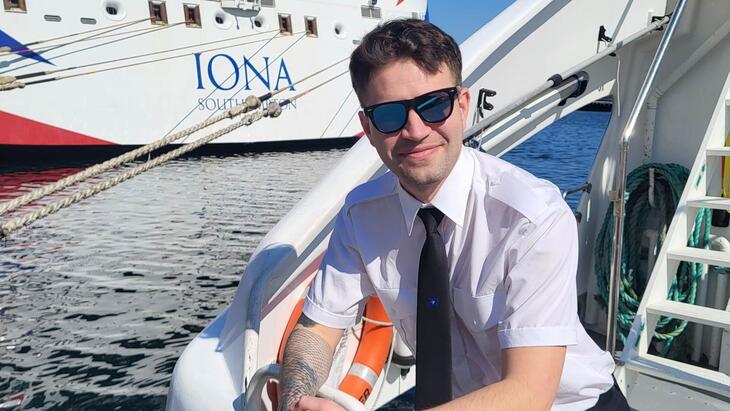 Boat employee on a sightseeing boat poses in front of a cruise ship