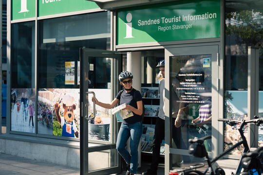 Kvinne på vei ut fra turistkontoret i Sandnes med sykkelhjelm på hodet og kart i hendene, klar for en sykkeltur
