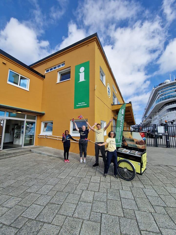 Fire personer vifter med brosjyrer i været utenfor turistinformasjonen i Stavanger