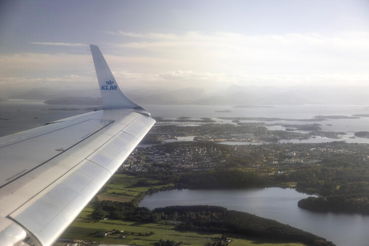 Bildet av en flyvinge fra vinduet av et fly. Man skimter Stavanger-regionen under. 