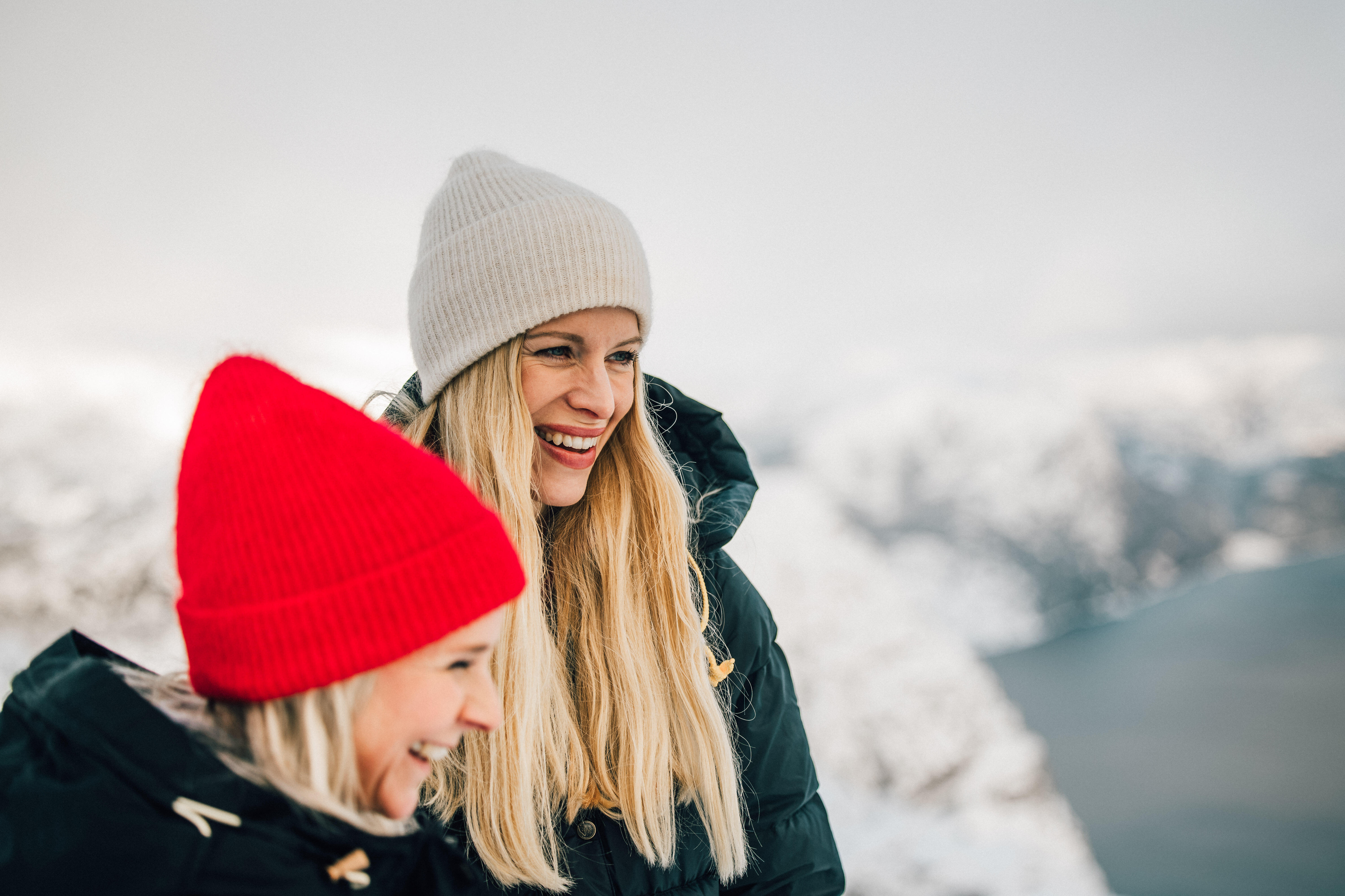 To damer står på fjelltopp med vinterlandskap bak seg